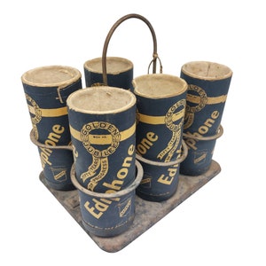 May include: A set of six black and gold cardboard tubes with the word "Edphone" printed on them. The tubes are arranged in a circular pattern on a wooden stand. The tubes are labelled with the words "Golden Jubilee", "Fifty Years of Progress", and "Box No."