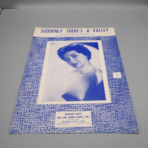 May include: Sheet music titled "Suddenly There's a Valley" featuring a black and white photo of a woman. The cover has a blue patterned border and includes the names of the songwriters and publisher.