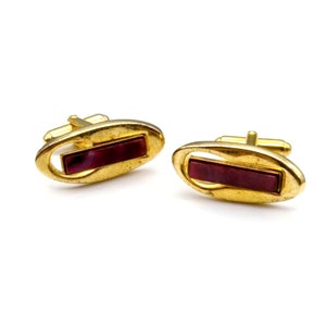 May include: A pair of gold cufflinks with a rectangular red stone inlay.