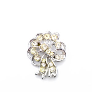 May include: A silver-toned brooch shaped like a bow with clear and yellow rhinestones.