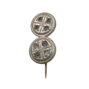May include: A silver pin with two round, decorative heads. Each head features a cross design with four clear stones.