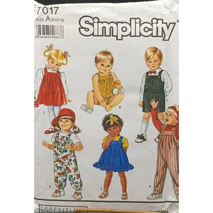 Pode incluir: Padrão de costura Simplicity com ilustrações de roupas infantis. O padrão inclui um vestido vermelho com babador, um macacão amarelo, macacões e um vestido azul. O tamanho do padrão é A (1/2-3).