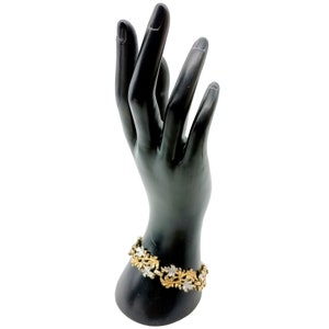 Può includere: Un braccialetto in oro e argento con un design a foglia. Il braccialetto è su una mano di manichino nera.