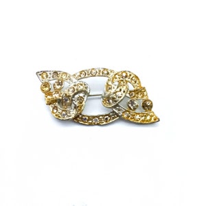 May include: A gold and silver tone brooch with a swirling design and clear rhinestones.
