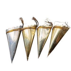 Puede incluir: Cuatro adornos metálicos en forma de cono. Dos son dorados, uno plateado y otro una mezcla de oro y plata. Cada uno tiene un borde festoneado y un lazo de alambre retorcido para colgar. Para decoraciones festivas.