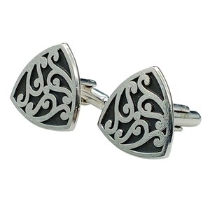 May include: A pair of silver-toned cufflinks with a triangular shape. Each cufflink features a black, ornate, swirling design within the silver frame. The cufflinks are connected by a silver bar.