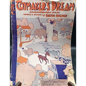 以下が含まれることがあります： 「The Toymaker's Dream」というタイトルのヴィンテージ楽譜の表紙。漫画の動物や建物のイラストが描かれています。タイトルと作曲者の名前はオレンジと青で表示されています。出版社の詳細は表紙の下部にあります。