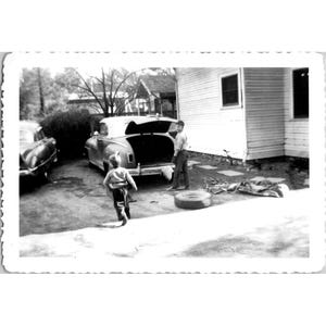 Vintage photo noir et blanc de garçons avec une voiture classique dans leur jardin, décembre 1954