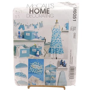 May include: A McCall's Home Decorating sewing pattern, featuring various home decor items. The pattern includes instructions for an apron, storage bins, and other accessories. The cover displays a blue and white floral apron and other items.
