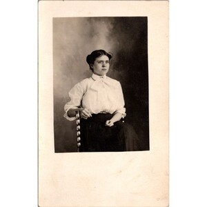 Carte postale ancienne de portrait RPPC, belle jeune femme dans une chaise de studio en laiton et parure