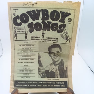 May include: A vintage magazine cover featuring a black and white photo of a man playing a guitar. The cover is titled "Cowboy Songs" and features the text "Greatest Collection Hill-Billy Western Songs".