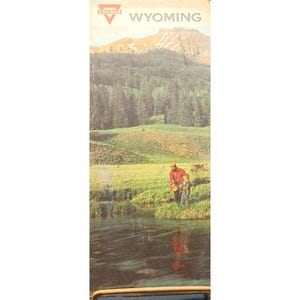 May include: Vintage travel advertisement for Wyoming featuring a scenic landscape with mountains, a forest, and a river. The advertisement includes the Conoco logo and the state name. A person in a red shirt and hat is fishing with a child.