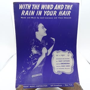 May include: A vintage sheet music cover with a purple background featuring a woman singing. The title of the song is "With the Wind and the Rain in Your Hair" by Jack Lawrence and Clara Edwards. The sheet music was introduced and recorded by Kay Kyser and his Orchestra featuring Ginny Simms on Columbia Records.