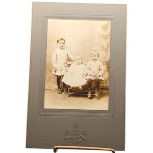 Retrato vintage en tonos sepia de tres niños en un marco de cartón repujado.