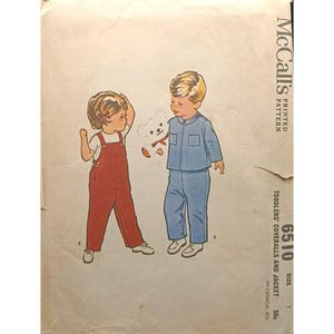 Puede incluir: Patrón de costura vintage McCall's para monos y chaqueta de niños pequeños. La ilustración muestra a dos niños, uno con un mono rojo y el otro con una chaqueta y pantalones azules, sosteniendo un osito de peluche. El número de patrón es 6510.