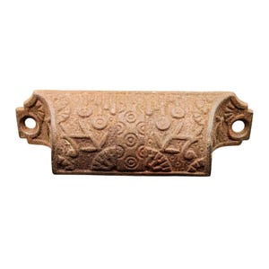 Può includere: Una maniglia per cassetto in ghisa vintage con un design decorativo di cerchi e volute. La maniglia è marrone e ha una finitura leggermente arrugginita.