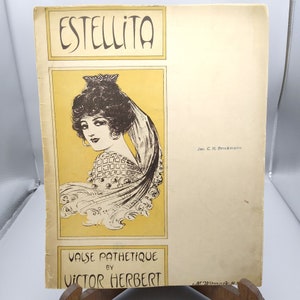 Puede incluir: Una portada de partitura musical vintage para la canción "Estelita" de Victor Herbert. La portada presenta una ilustración en blanco y negro de una mujer con velo, vestida con un vestido estampado. El texto "Valse Pathetique" está impreso debajo de la ilustración.
