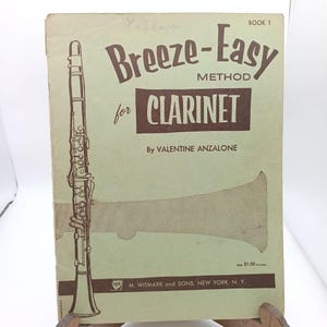 Puede incluir: Partitura antigua titulada "Breeze-Easy Method for Clarinet" de Valentine Anzalone. La portada presenta una ilustración marrón de un clarinete y su campana sobre un fondo verde claro. El libro está marcado como "Book 1".
