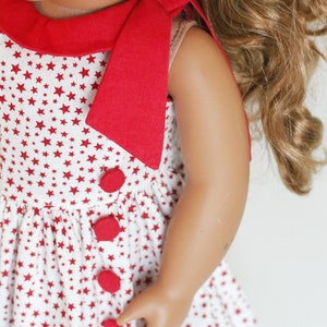 May include: A red and white sleeveless dress with a red bow at the neck and red buttons down the front. The dress is covered in a white background with red stars.