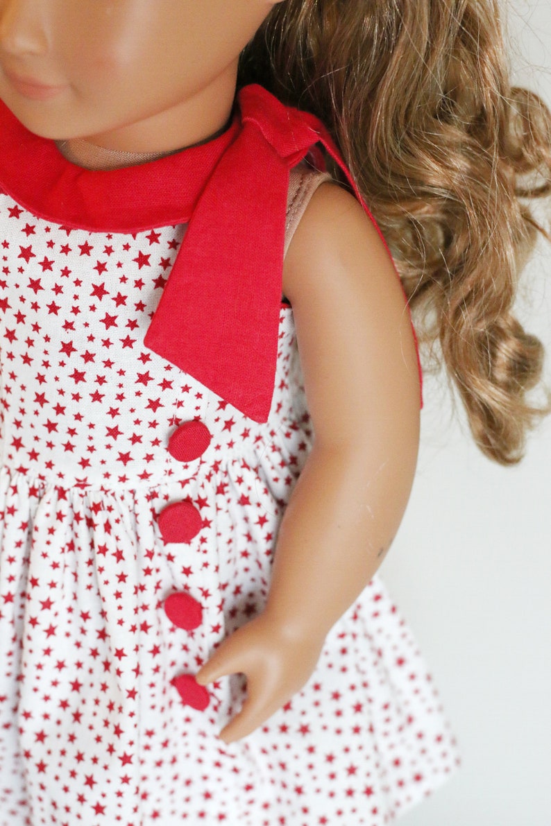 May include: A red and white sleeveless dress with a red bow at the neck and red buttons down the front. The dress is covered in a white background with red stars.