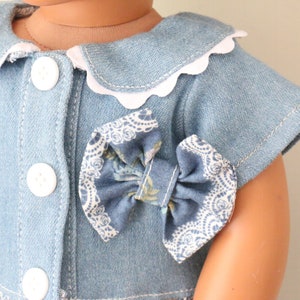 May include: A blue denim dress with a white scalloped collar and a blue and white floral bow.
