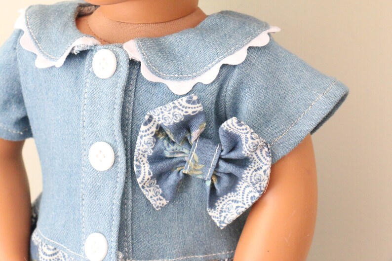 May include: A blue denim dress with a white scalloped collar and a blue and white floral bow.