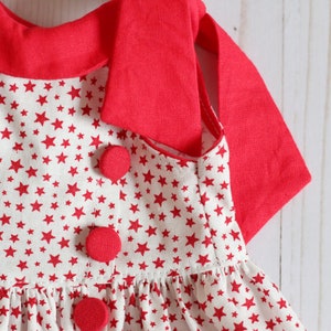 May include: A red and white sleeveless dress with a red collar and red buttons. The dress has a white background with a red star pattern.