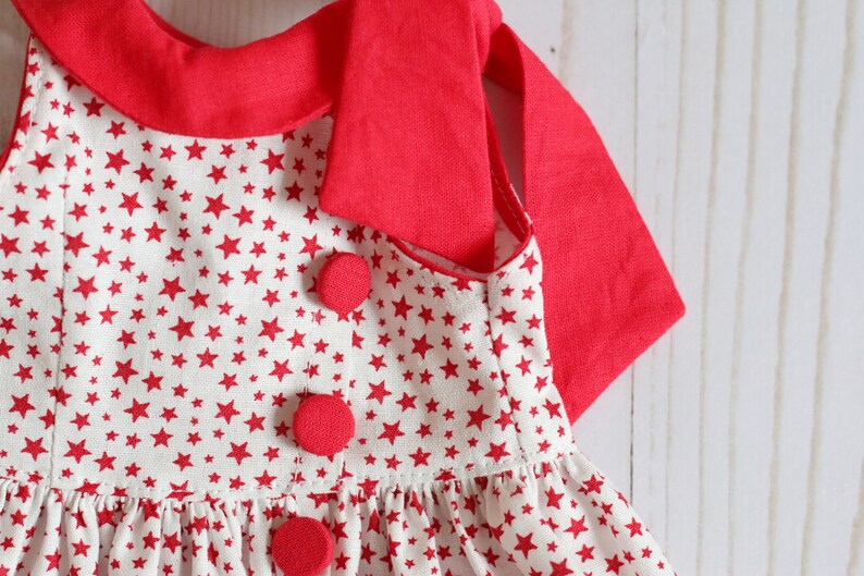 May include: A red and white sleeveless dress with a red collar and red buttons. The dress has a white background with a red star pattern.
