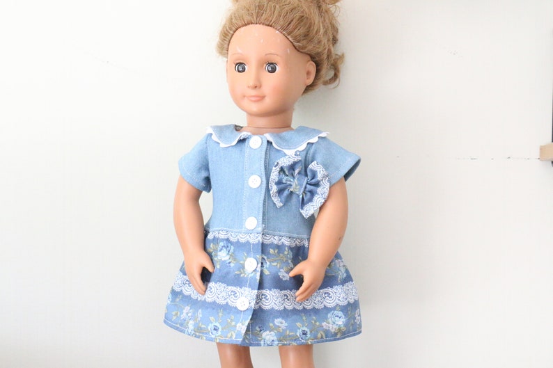 May include: A blue denim dress with a white collar and a floral print skirt. The dress has a bow on the front and white buttons.