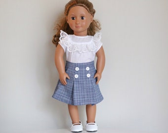 May include: A doll wearing a white blouse with a lace collar and a blue plaid skirt with white buttons. The doll has brown hair and brown eyes.