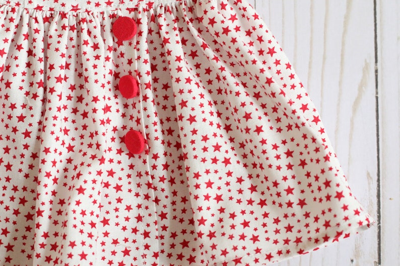 May include: A white skirt with a red star pattern and three red buttons.