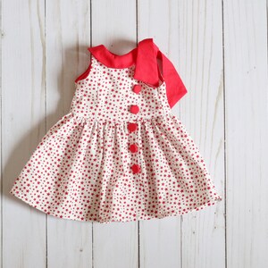 May include: A red and white sleeveless dress with a red bow at the neck and red buttons down the front. The dress is covered in a small red star pattern.