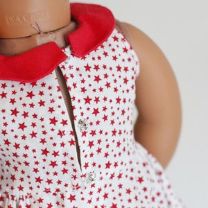 May include: A white sleeveless dress with a red collar and red stars printed all over. The dress has a button closure in the front.