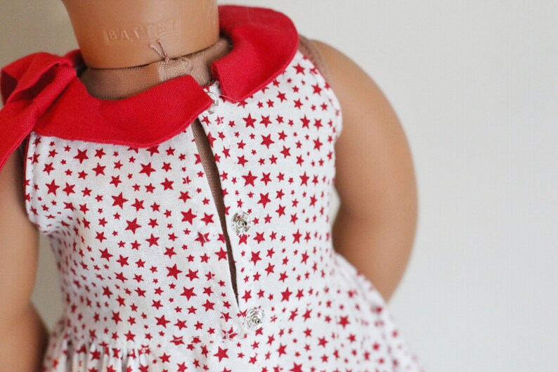 May include: A white sleeveless dress with a red collar and red stars printed all over. The dress has a button closure in the front.