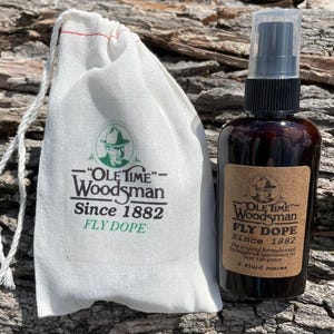 May include: A brown glass spray bottle and a white drawstring bag with the text "OLE TIME Woodsman Since 1882 FLY DOPE". The bottle has a label with the same text and the words "2 fluid ounces". The bag is next to the bottle.