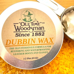 May include: A round metal tin of "Ole Time" Woodsman Dubbin Wax, a product for restoring and waterproofing leather boots and gloves. The tin is on a wooden surface, with a scoop of white wax and yellow wax beads.