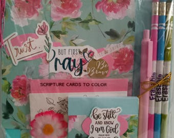 May include: A gift set with a floral theme, including a journal, scripture cards, pens, and pencils. The journal has a teal background with pink flowers and the words "Trust" and "Pray". The set also includes a pink flower and the text "Be still and know I am God".