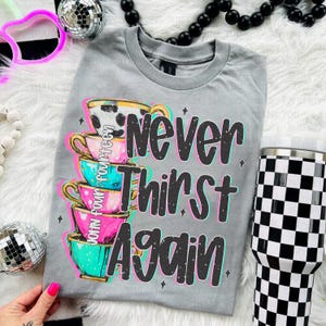 May include: Gray t-shirt with a stack of teacups and the text "Never Thirst Again".