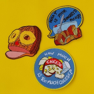 Puede incluir: Tres parches bordados para planchar con un tema de comida. Un parche es una burbuja de diálogo con el texto "¿Cuál es tu política de espaguetis?" y una imagen de dibujos animados de espaguetis. Otro parche es una burbuja de diálogo con el texto "¿Cuánto queso es demasiado queso?" y una imagen de dibujos animados de queso. El tercer parche es una imagen de dibujos animados de un jamón con boca y ojos.