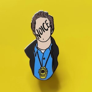 Peut inclure: Une épingle en émail représentant un homme de dessin animé avec le mot "NOICE" qui lui couvre le visage. Il porte une chemise bleue, une veste noire et une chaîne en or avec un badge jaune.