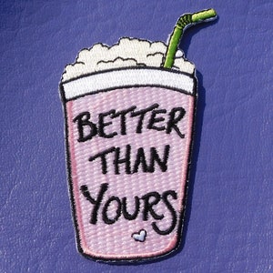 May include: Pink and white embroidered patch of a milkshake with a green straw and the text "Better Than Yours" with a small pink heart.