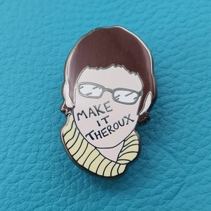 May include: A silver enamel pin featuring a cartoon illustration of a person with brown hair, glasses, and a yellow striped scarf. The text "MAKE IT THEROX" is written across the person's face.