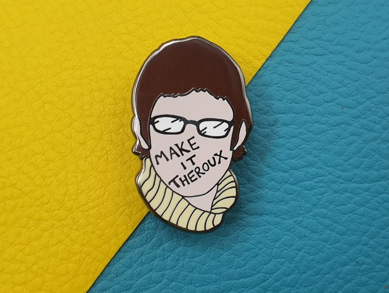 May include: A silver enamel pin featuring a cartoon illustration of a person with brown hair wearing glasses and a yellow and white striped scarf. The text "MAKE IT THEROX" is written across the person's face.