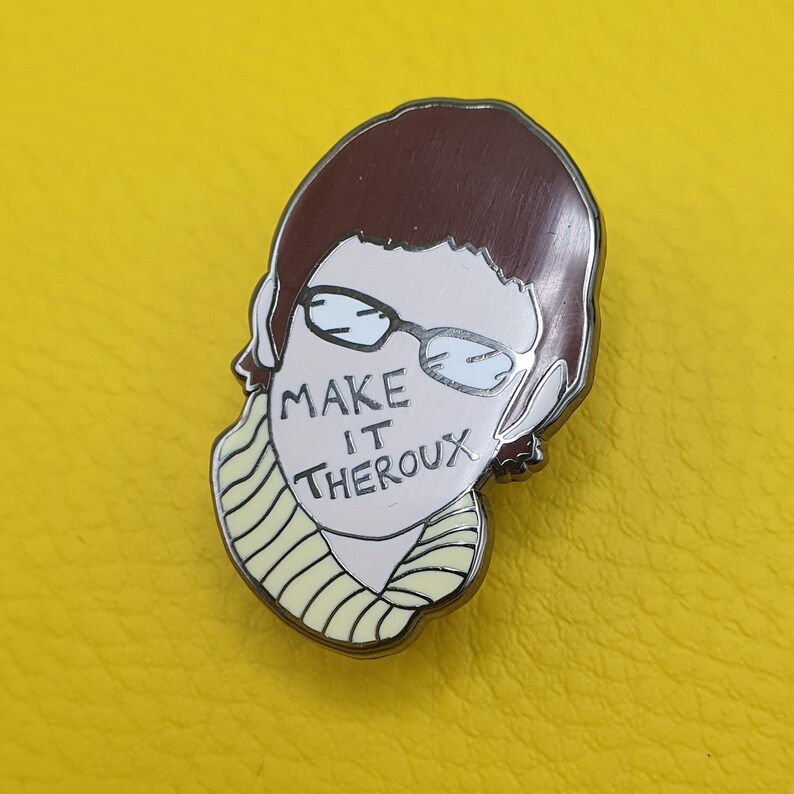 May include: A silver enamel pin featuring a cartoon illustration of a person with brown hair wearing glasses and a yellow scarf. The text "MAKE IT THEROX" is written on the person's face.