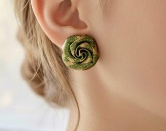 May include: A close-up of a green and gold rose-shaped stud earring. The earring features a detailed floral design with a spiral centre and layered petals. The earring is worn on an ear.