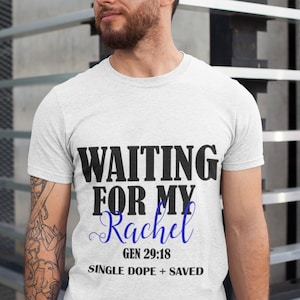 May include: Light gray t-shirt with the text "WAITING FOR MY Rachel" in black and blue. Below the text are the words "GEN 29:18" and "SINGLE DOPE + SAVED" in black.