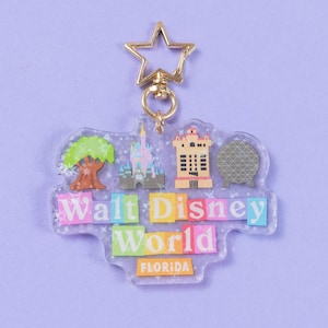 Puede incluir: Un llavero de acrílico transparente con las palabras "Walt Disney World" en letras coloridas. El llavero tiene un cierre dorado en forma de estrella e incluye ilustraciones en miniatura de un árbol, un castillo, un edificio y una esfera. La palabra "FLORIDA" está en la parte inferior.