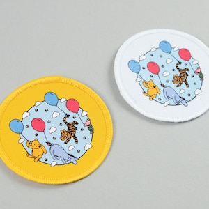 May include: Two circular patches featuring Winnie the Pooh characters. One has a yellow background, the other is white. Both have a blue sky background with red and blue balloons, and illustrations of Winnie the Pooh, Tigger, and Eeyore.