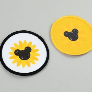 May include: Two round patches featuring a sunflower design with a black Mickey Mouse head in the center. One patch has a white background with a black border, the other is yellow.