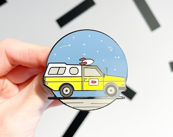 Puede incluir: Un pin de esmalte amarillo y azul que representa una furgoneta de dibujos animados con una tabla de surf en la parte superior, conduciendo por un cielo nocturno estrellado. La furgoneta tiene un techo blanco y una tabla de surf roja y blanca.